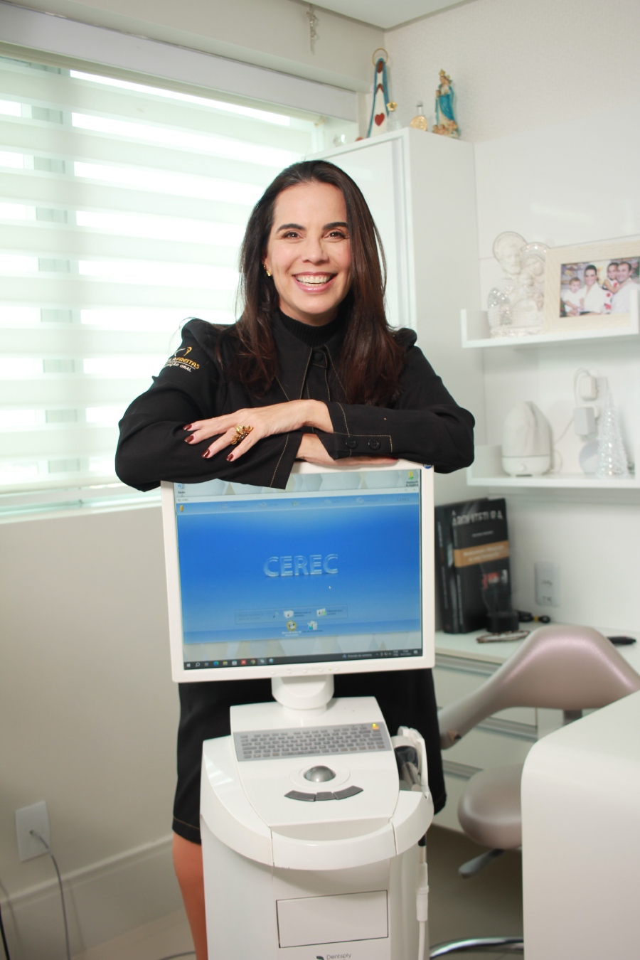 Dra. Camila Freitas sorrindo ao lado de um monitor com escaneamento digital 3D para planejamento de implantes zigomáticos em Feira de Santana.