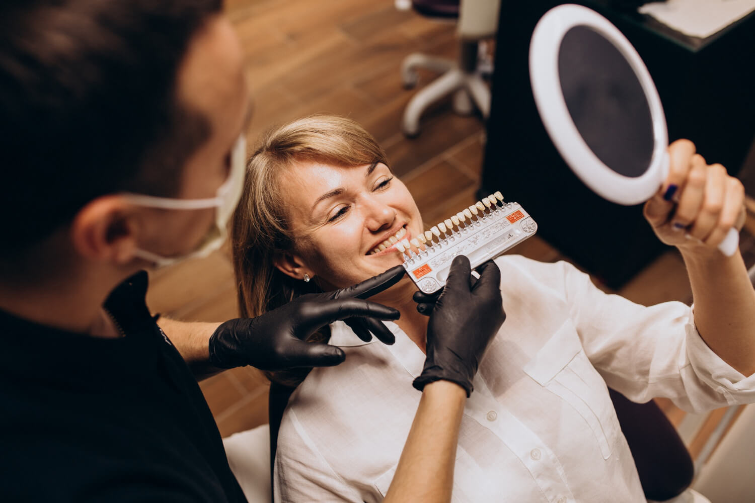 Paciente no consultório comparando escala de cores de dentes para aplicação de facetas em porcelana em Feira de Santana com Dra. Camila Freitas.