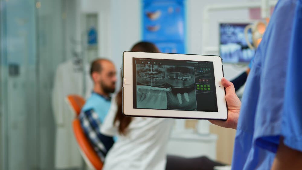 Dentista segurando tablet com radiografia digital e planejamento de implantes e alinhadores em Feira de Santana na clínica Dra. Camila Freitas.