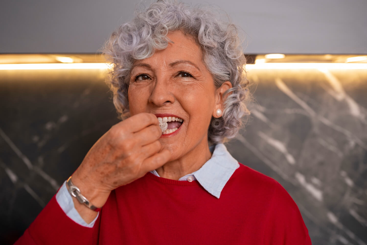 Senhora de cabelos grisalhos sorrindo ao comer, representando a recuperação da função mastigatória com implantes zigomáticos em Feira de Santana.