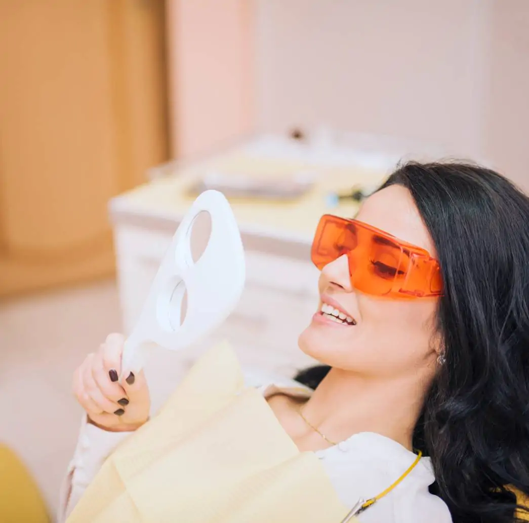 Paciente sorrindo ao observar resultado de lentes de contato dental no espelho. Estética dental em Feira de Santana com Dra. Camila Freitas.