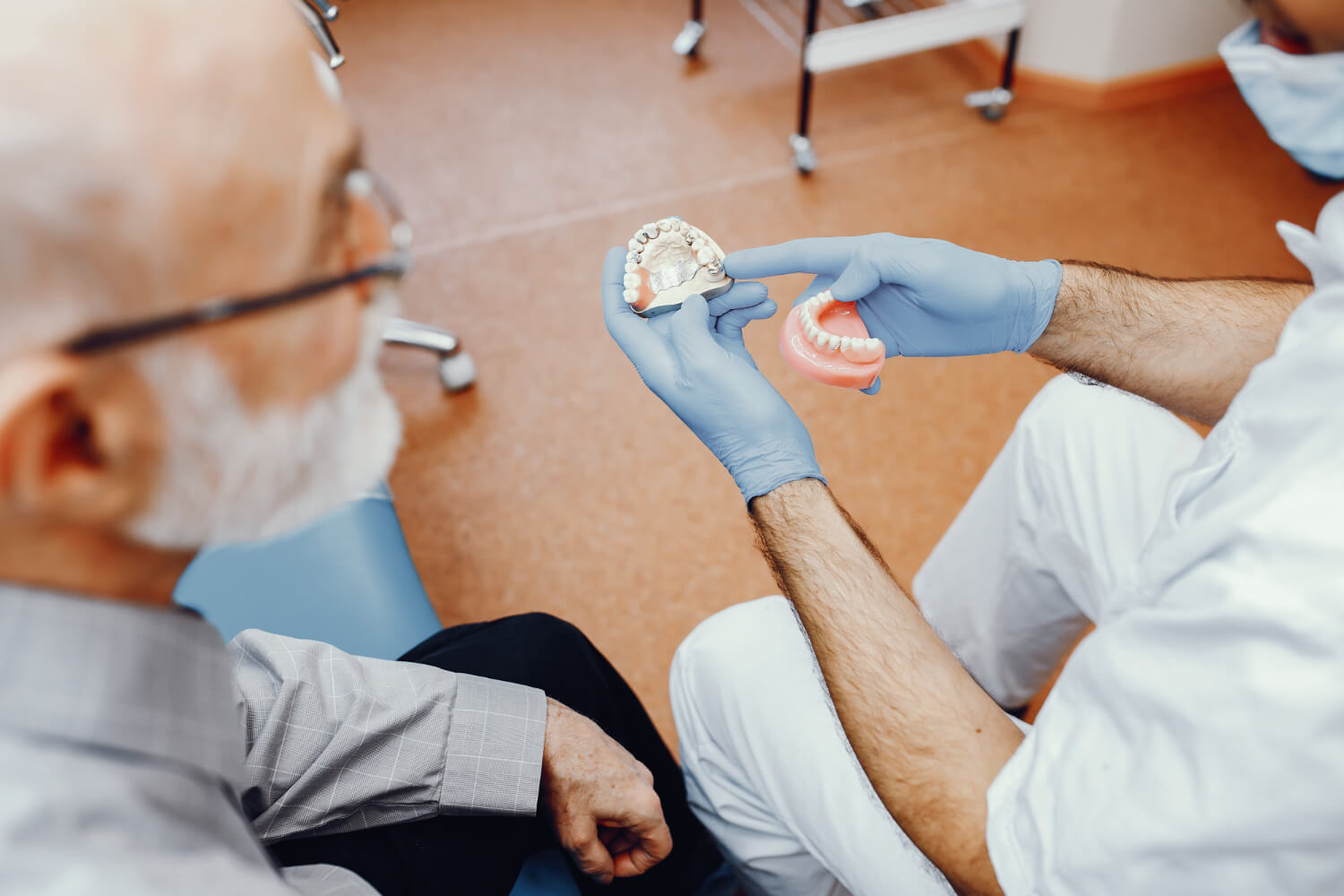 Dentista mostrando modelo de prótese protocolo fixa sobre implantes para paciente idoso em Feira de Santana na clínica Dra. Camila Freitas.